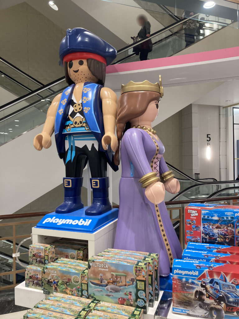 Two large Playmobile figurines sit on top of a shelf. The left one is a pirate, the right one a queen.