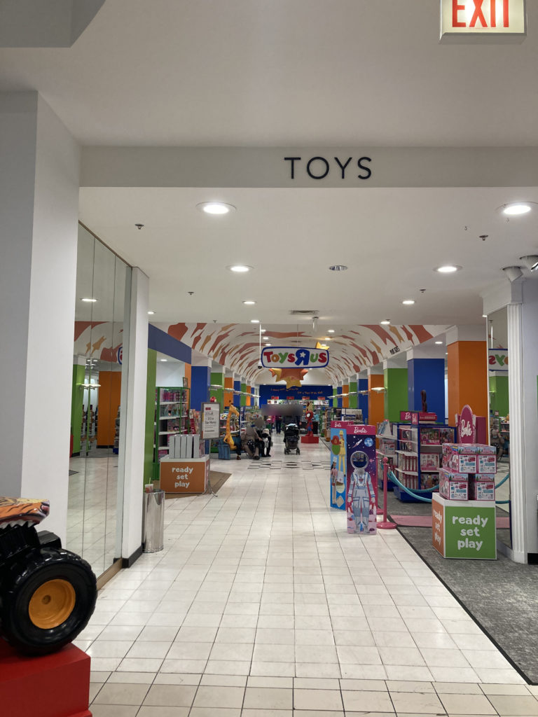 A photo showing the aisleway of the Toys R Us space. Above the entrance to the aisleway, there is a sign that says "TOYS" in Macy's lettering.